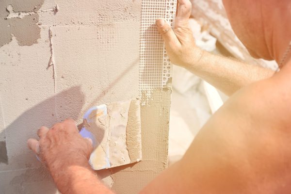 Fifty years old manual worker with wall plastering tools renovating house. Plasterer renovating walls and corners with spatula and plaster. Wall mash installation. Construction finishing works